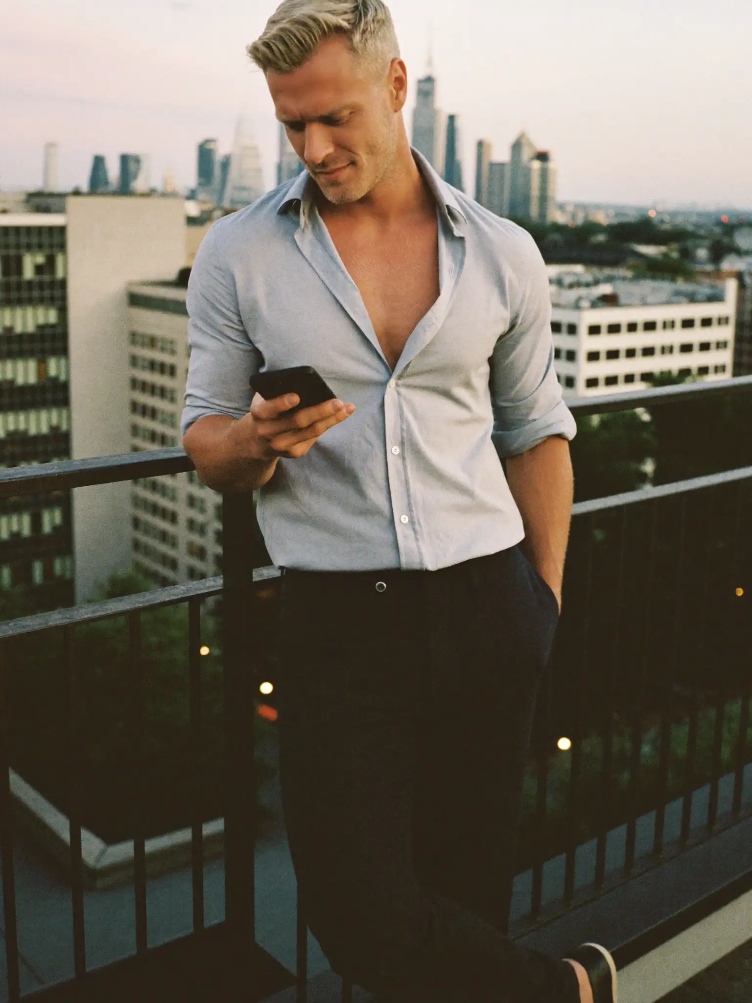 Mann tippt Flirt Nachricht vor Frankfurter Skyline bei Sonnenuntergang – Er sucht ihn Frankfurt Gay Dating Rooftop